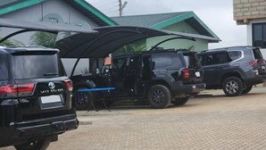 A parking area with several SUVs, a covered vehicle, and buildings with green roofs. - Tetra Jungle Lodge (Akropong)