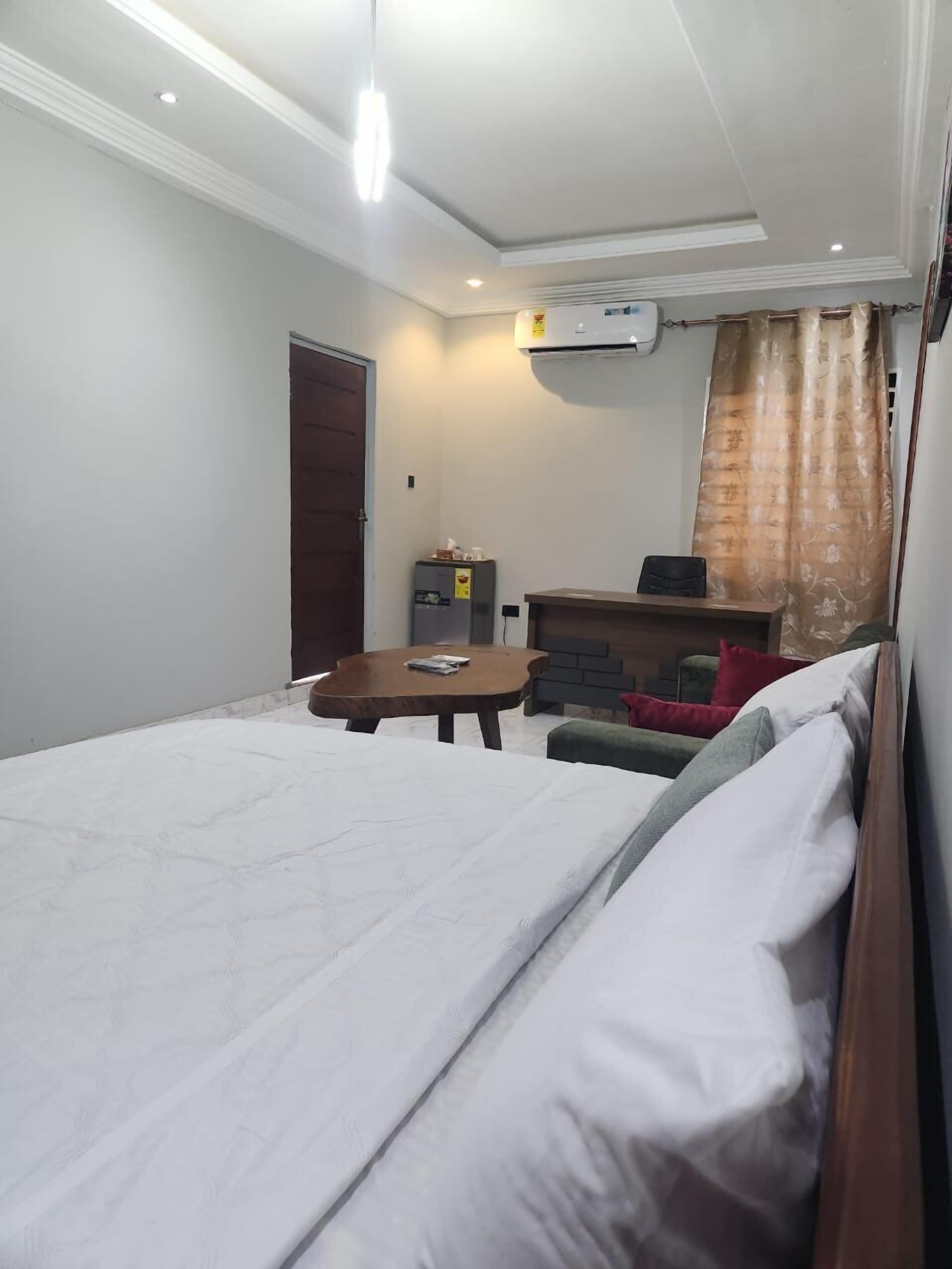 A hotel room with a bed, a small table, a desk, an air conditioner, and a curtain.