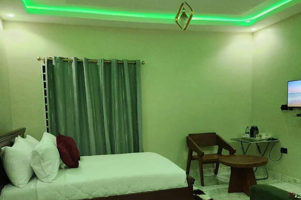 A bedroom with a bed, a chair, a small table, and a TV.