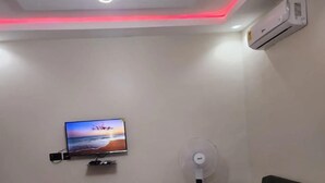 A modern living room with a flat-screen TV, a standing fan, a green sofa, and a marble-tiled floor. - Tetra Jungle Lodge (Akropong)