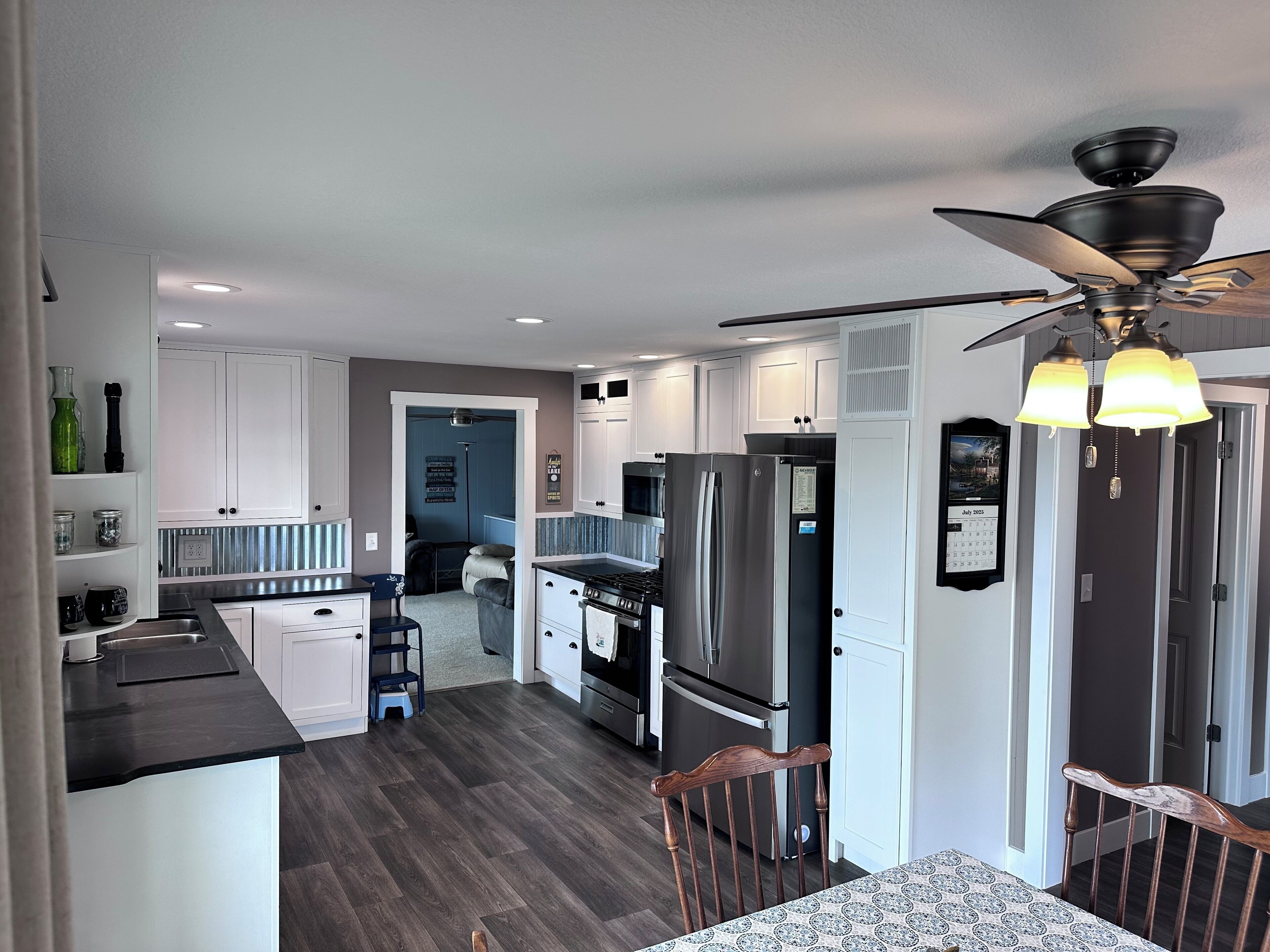 A modern kitchen with white cabinets, a black countertop, and a stainless steel refrigerator.