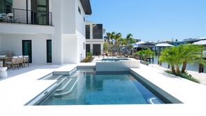 A modern pool area with a clear view of the pool, a dining area with outdoor furniture, and a view of the surrounding buildings and palm trees. - Madera Holiday Home (Fort Myers Beach)