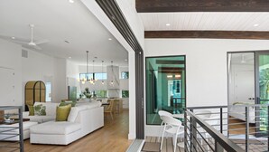 A modern living room with a white sofa, wooden flooring, and a balcony with a railing. - Madera Holiday Home (Fort Myers Beach)