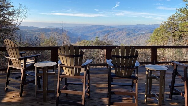 A deck with four Adirondack chairs and a small table, overlooking a mountainous landscape.