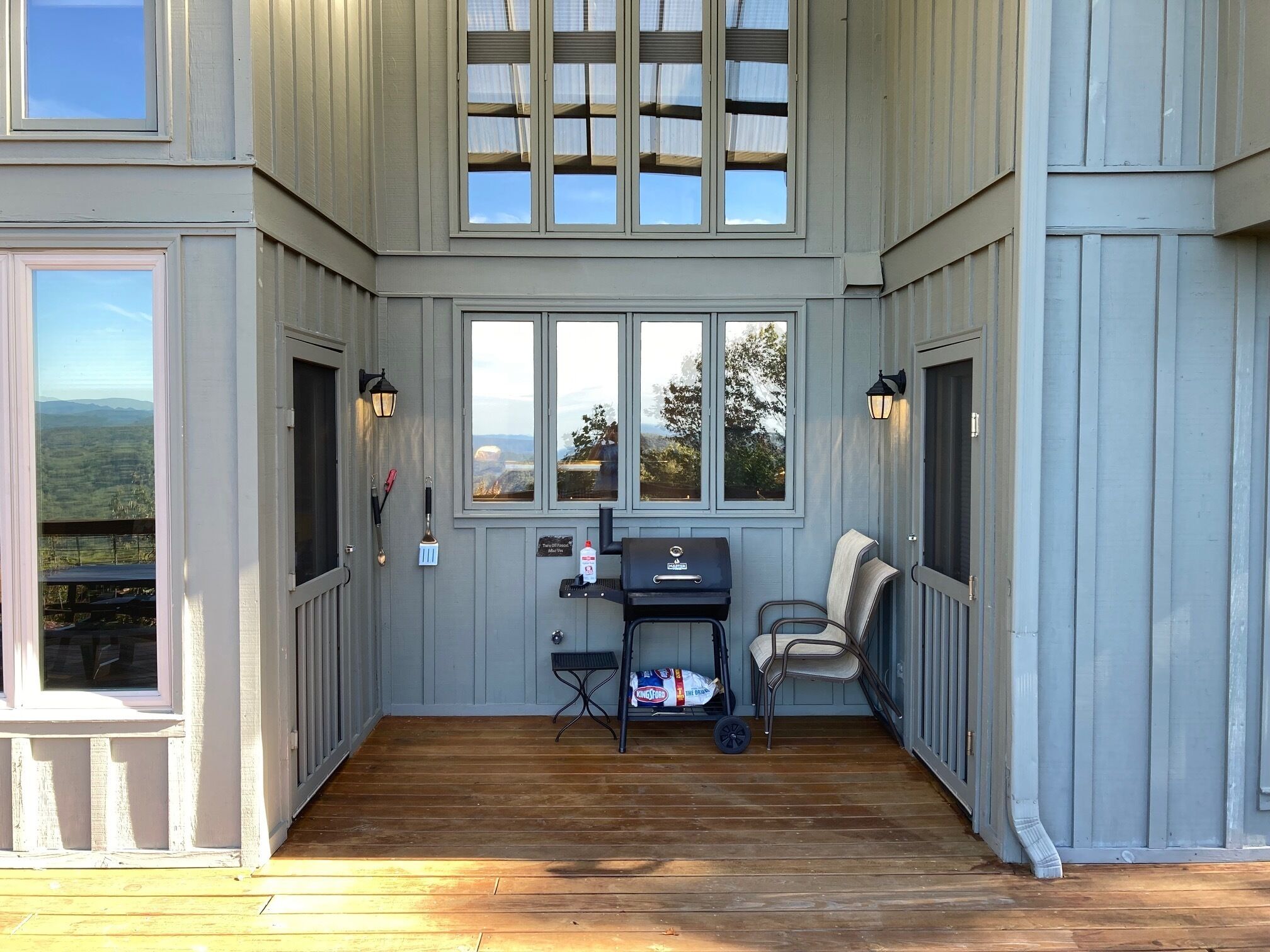 A covered porch with a grill, outdoor seating, and large windows offering views of the landscape.