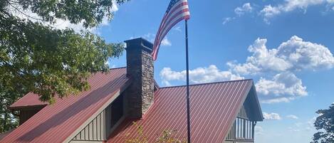 A two-story building with a stone chimney, a metal roof, and an American flag.