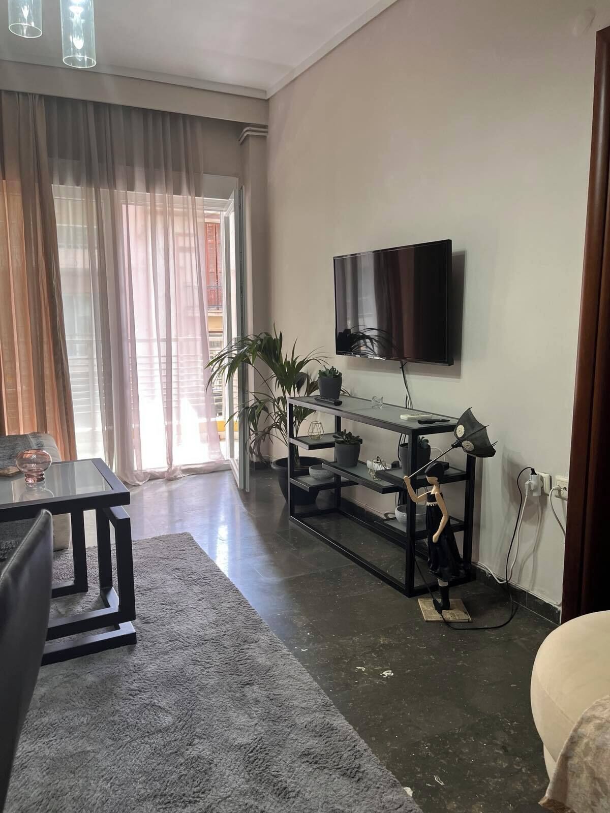 A living room with a flat-screen TV mounted on the wall, a glass coffee table, a sofa, and a small table with decorative items.