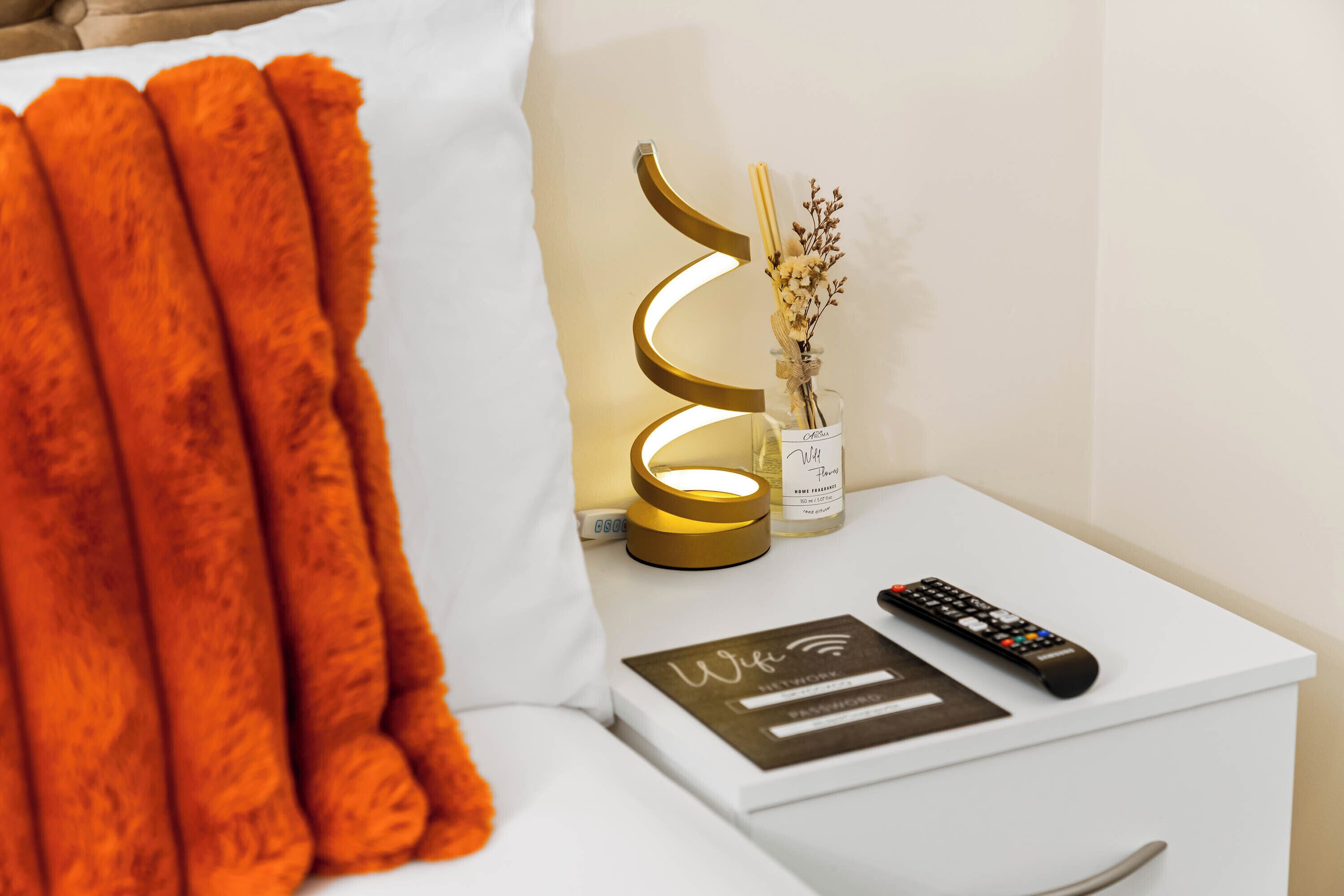 A white bedside table with a remote control, a decorative item, and a small vase with dried flowers.