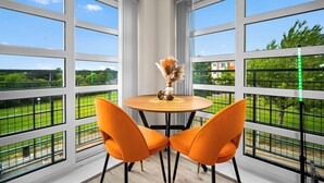Ein Zimmer mit großen Fenstern, einem runden Holztisch und zwei orangefarbenen Stühlen.
