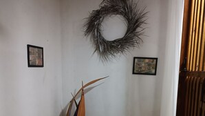 A bedroom with a bed, two pillows, a wooden headboard, a wall-mounted wreath, and two framed pictures.