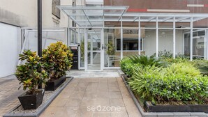 Een modern gebouw met een glazen ingang, omringd door verzorgde beplanting en een geplaveid pad.