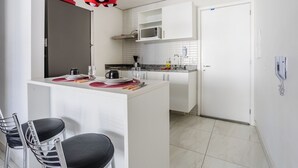 Een kleine keuken met witte kasten, een magnetron en een rode hanglamp.