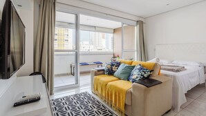 Een hotelkamer met een bank, een bed, een televisie en een balkon met uitzicht op de stad.