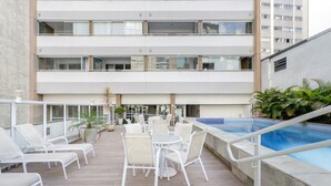 Een terras op het dak met een zwembad, lounge stoelen en plantenbakken.