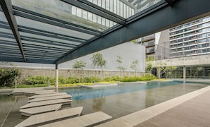 A modern indoor pool area with a glass ceiling, surrounded by greenery and a view of a high-rise building. - Modern Studio in Itaim Bibi-sp Cia2313 (São Paulo)
