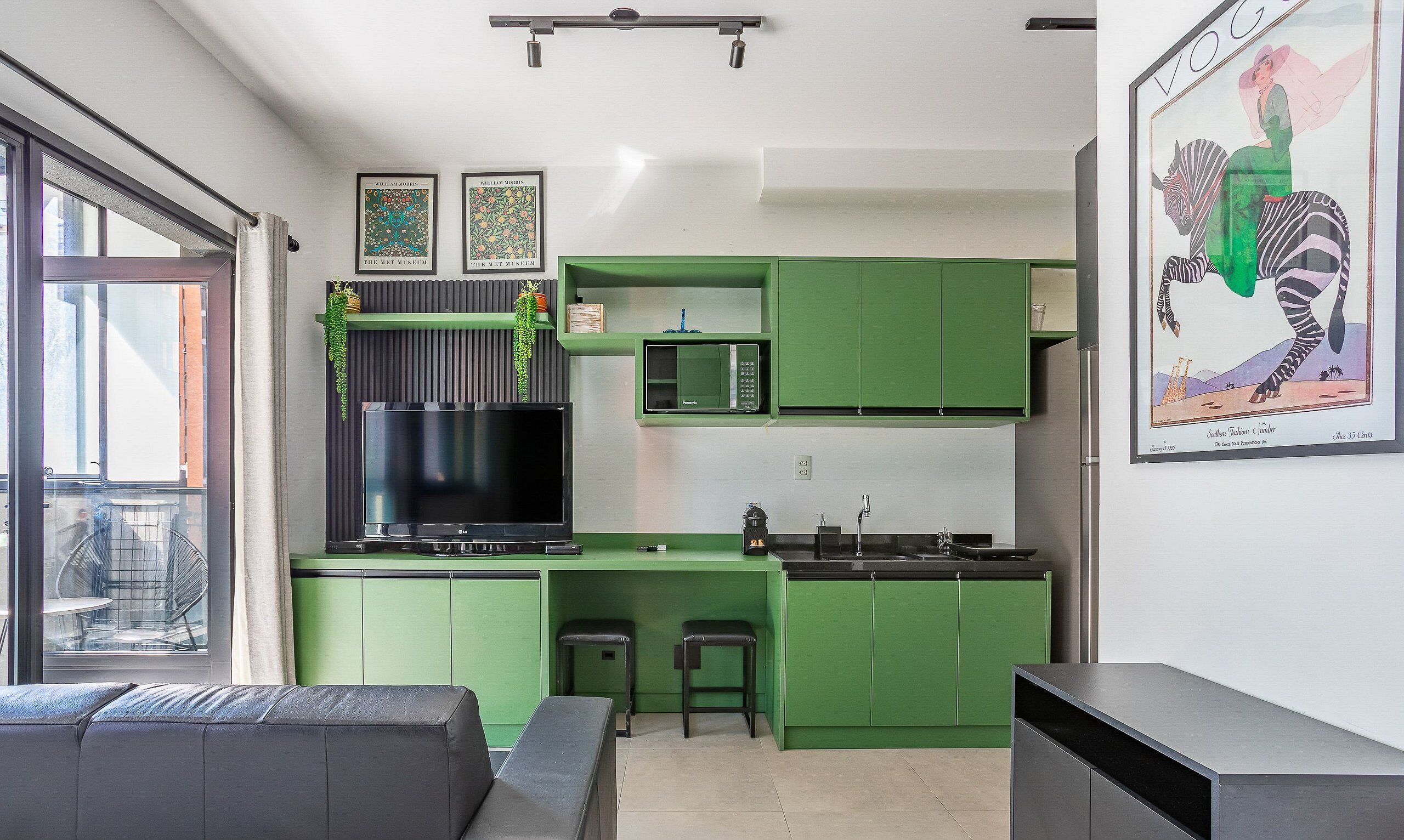 Une cuisine moderne avec des meubles de couleur verte, un téléviseur à écran plat et un coin repas comprenant un canapé et des fauteuils.