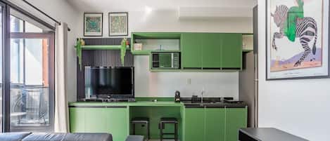 A modern kitchen with green cabinets, a flat-screen TV, and a dining area with a sofa and chairs.