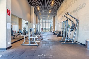 Une salle de sport moderne dotée de divers appareils d’exercice, de grandes fenêtres et d’un plafond haut avec un éclairage linéaire.