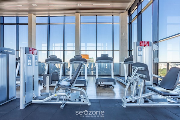 A gym with various exercise machines, large windows, and a modern design.