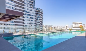 A modern hotel with a rooftop infinity pool, glass railings, and a cityscape view.