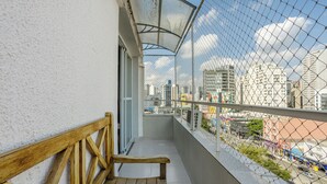 A balcony with a wooden bench, a metal railing, and a view of a cityscape through a chain-link fence. - Charming Apartment in Pinheiros - Cot0081 (São Paulo)