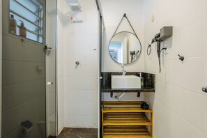 A bathroom with a glass shower enclosure, a sink with a mirror above it, and a towel rack. - Charming Apartment in Pinheiros - Cot0081 (São Paulo)