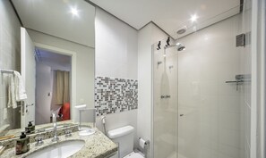 Un baño moderno con lavamanos de granito, inodoro, ducha con puerta de vidrio y un respingo de mosaico.
