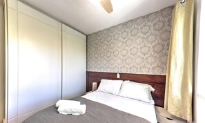 Un dormitorio con cama, mesita de noche, armario y papel tapiz estampado.