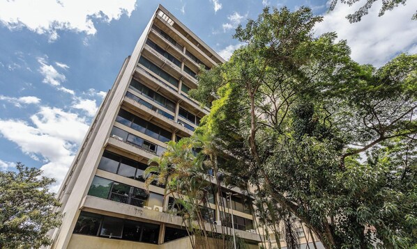 A multi-story building with balconies and large windows, surrounded by trees.