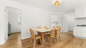 Une cuisine moderne avec des meubles blancs, une table à manger en bois et six chaises en osier, et un four visible.