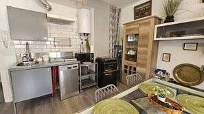 Une cuisine compacte dotée d’appareils électroménagers modernes, un coin repas avec une table et des chaises, et un meuble en bois avec des portes en verre.
