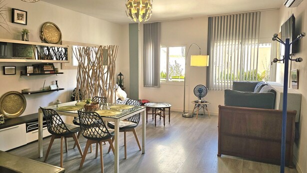 A modern living room with a dining area, a sofa, and a TV mounted on the wall.