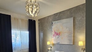 A modern bedroom with a large bed, two bedside lamps, a decorative ceiling light, and a large abstract painting on the wall.