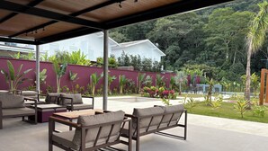 An outdoor patio area with seating and a view of a white house and lush greenery. - House with 4 bedrooms in the best gated community in Maresias, 150 meters from the beach. (Maresias São Sebastião)