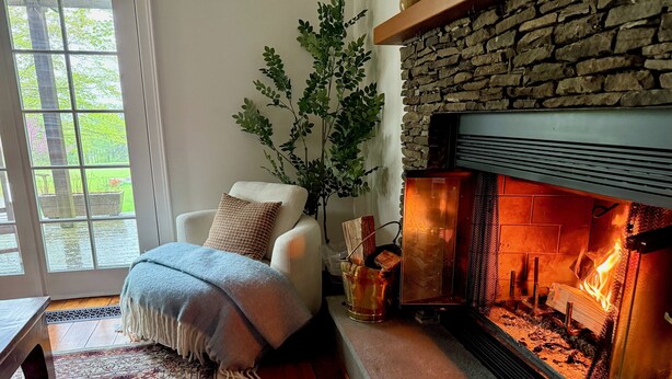 Un salón acogedor con chimenea, un sillón cómodo, un ventanal grande y una planta decorativa.
