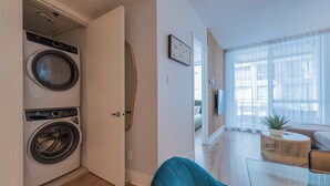 Eine moderne Wohnung mit Waschmaschine, einem Essbereich mit Glastisch und einem Wohnzimmer mit Sofa und Pflanze.