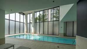 Ein Innenpool mit großen Glaswänden, gefliestem Boden und Liegestühlen.