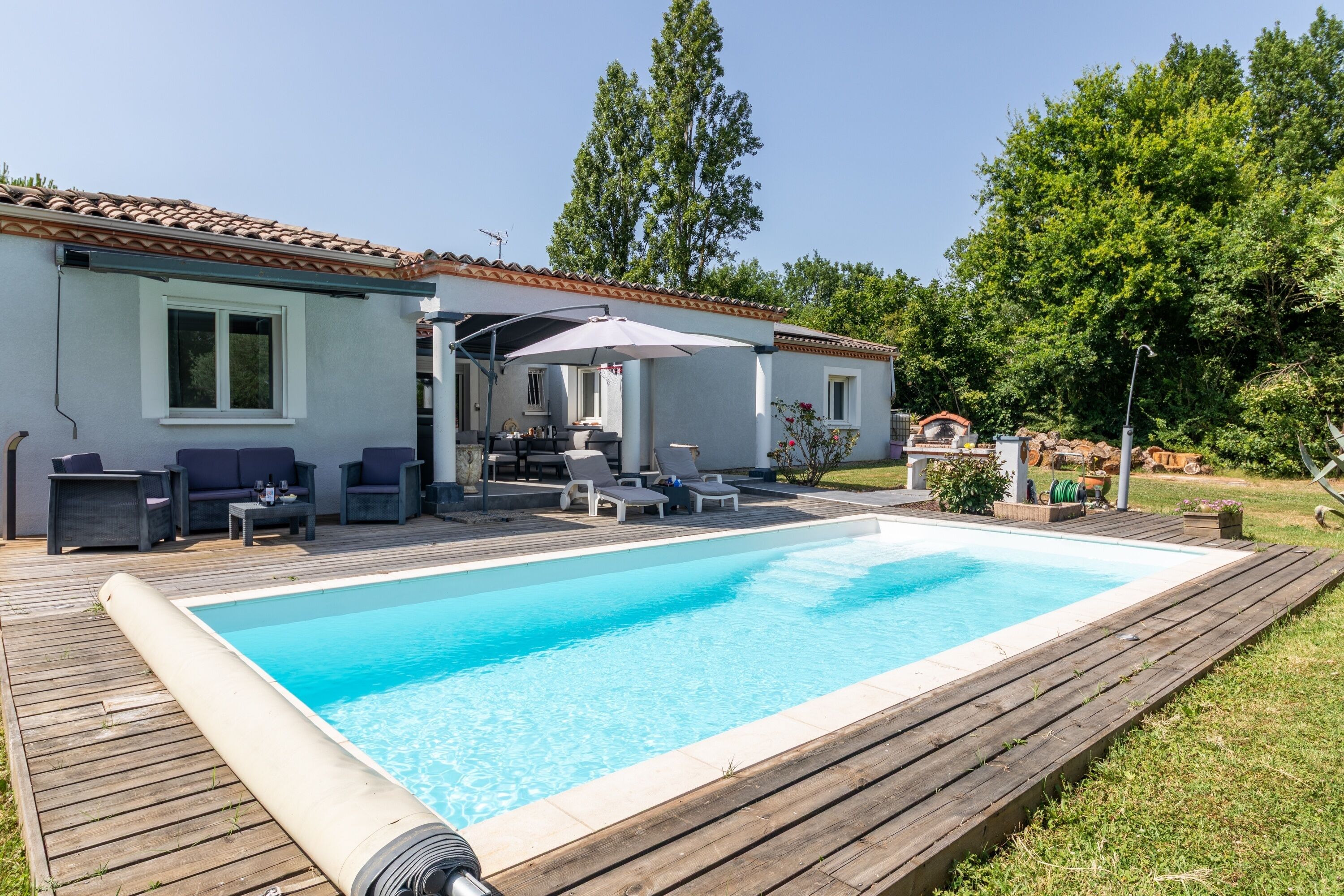 A swimming pool with a wooden deck, outdoor furniture, and a covered patio area.