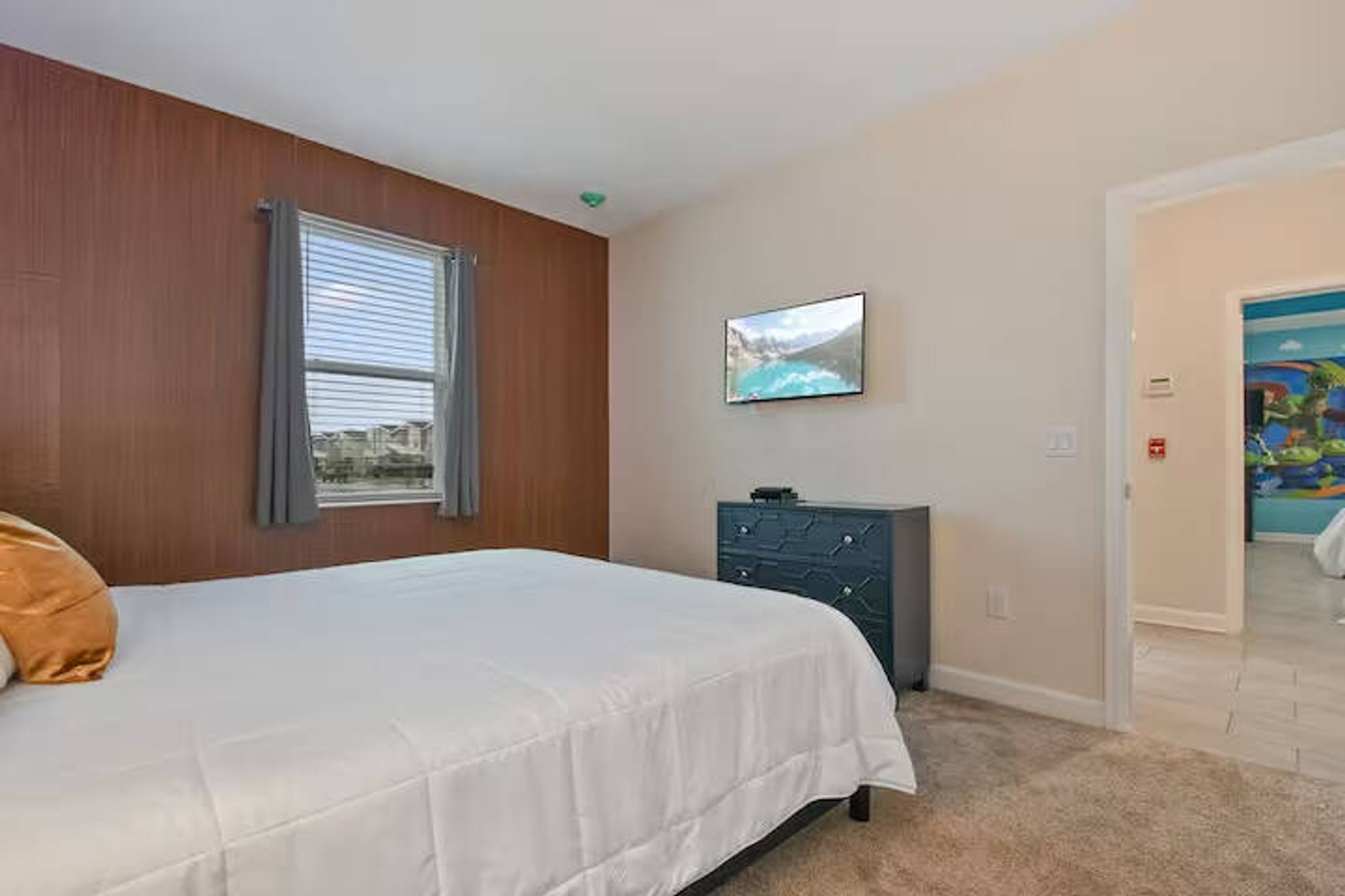 Een slaapkamer met een bed, een kast, een televisie en een deur naar een andere kamer.