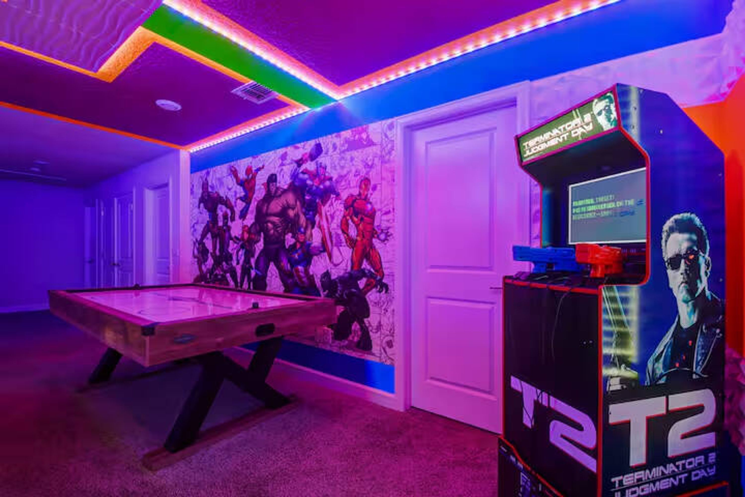 Une pièce équipée d’une table de billard, d’une borne d’arcade de type T2 et ornée d’une fresque murale.