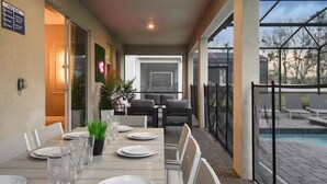 An outdoor dining area with a pool view, tables set with plates and glasses, and a glass-enclosed patio. - Lakeview 9bedroom Home Private Pool Game Theater (Kissimmee)
