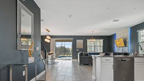 A modern kitchen with a dishwasher, a dining area with a glass table, and a staircase leading to another level. - Lakeview 9bedroom Home Private Pool Game Theater (Kissimmee)