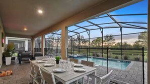 An outdoor dining area with a pool view, covered patio, and seating. - Lakeview 9bedroom Home Private Pool Game Theater (Kissimmee)