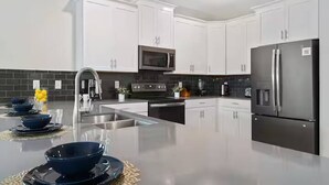 A modern kitchen with white cabinets, stainless steel appliances, and a central island with seating. - Lakeview 9bedroom Home Private Pool Game Theater (Kissimmee)