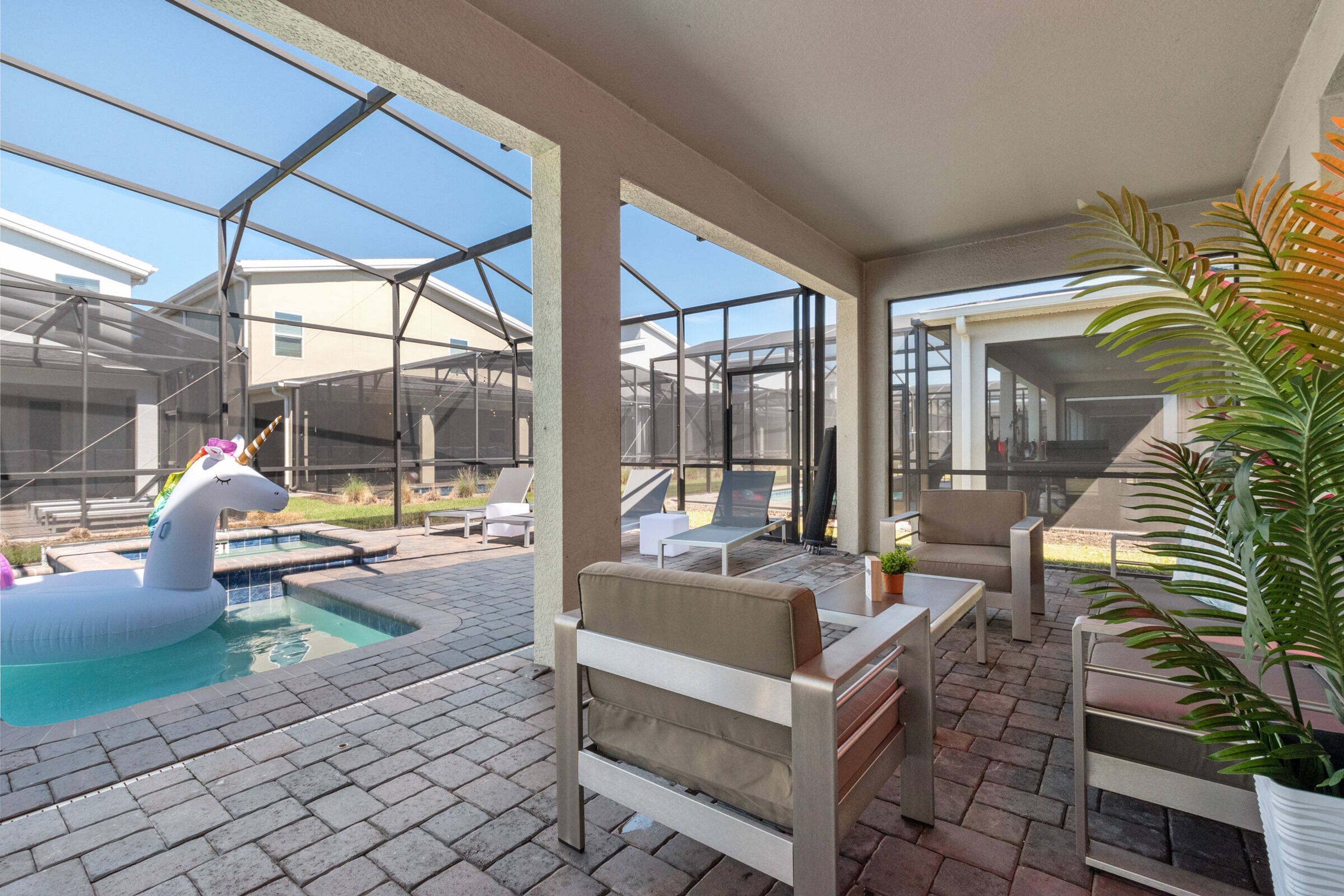 A covered outdoor patio with a swimming pool, lounge chairs, and a decorative unicorn float.