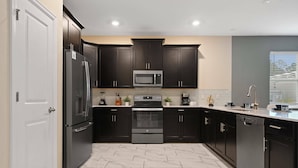 A modern kitchen with dark cabinetry, stainless steel appliances, and a tiled floor. - Gorgeous 9bedroom Home Private Pool Game Theater (Kissimmee)
