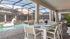 A covered outdoor dining area with a pool, white dining tables, and chairs. - Gorgeous 9bedroom Home Private Pool Game Theater (Kissimmee)