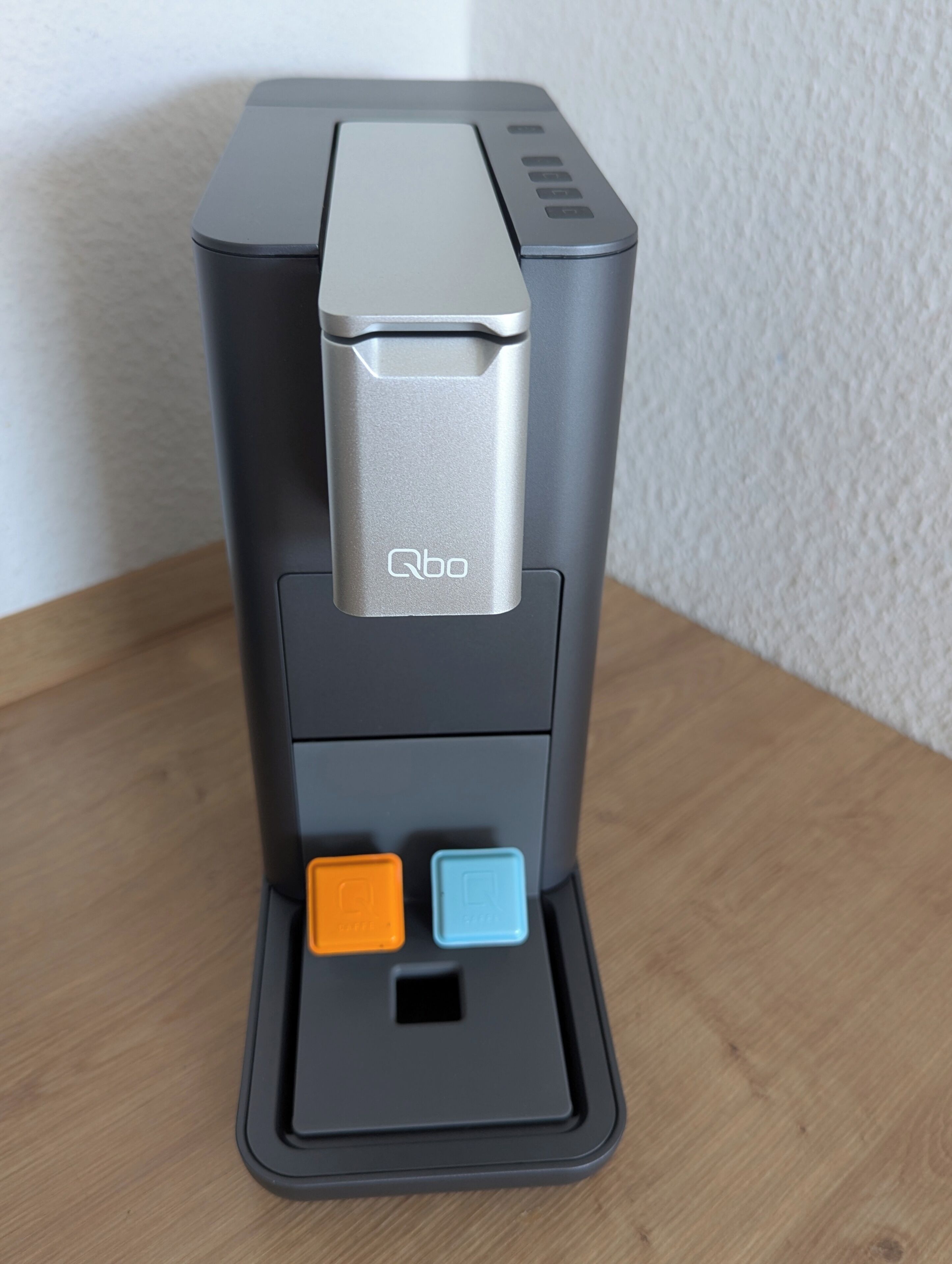 A coffee machine with a silver top, a brand logo, and two buttons below it.