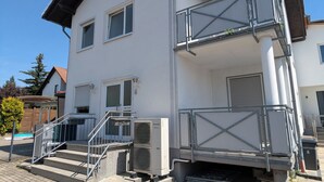 Um edifício de dois andares com varanda, escadaria e unidade de ar condicionado visível.