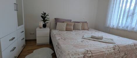 Un dormitori amb llit, una nit, una commode, una planta en test i una finestra amb cortines.